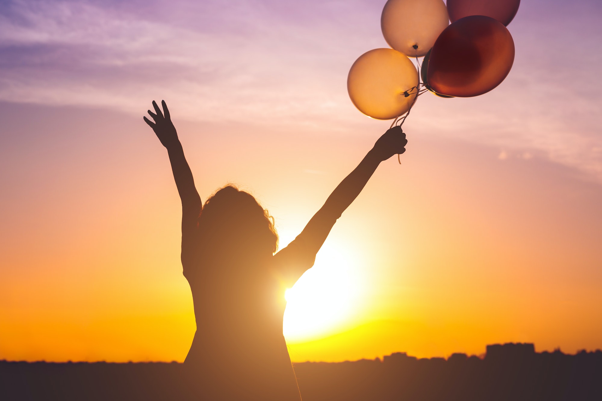 Happy woman with balloons at sunset